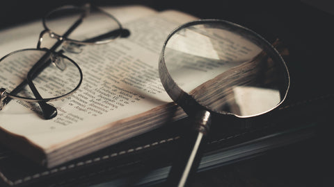 A pair of round glasses sitting on a book with a magnifying glass