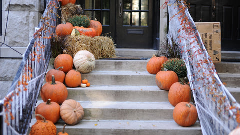 Stairs going up to a front porch decorated for Halloween with pumpkins, hay, and fake cobwebs and orange decorations on the banister