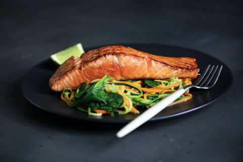 A plate of salmon on a bed of vegetables.