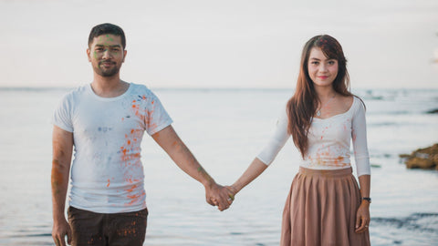 Man and woman holding hands on the beach looking at camera