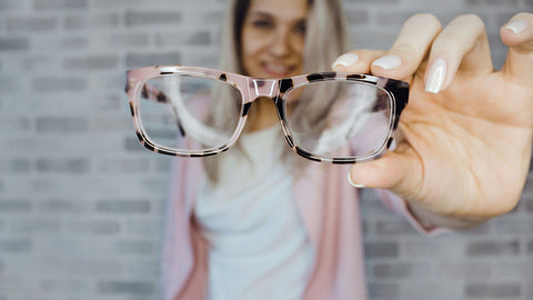 A woman holding pink glasses close to the camera. Give someone with Low Vision a New Beginning with Vision Buddy!