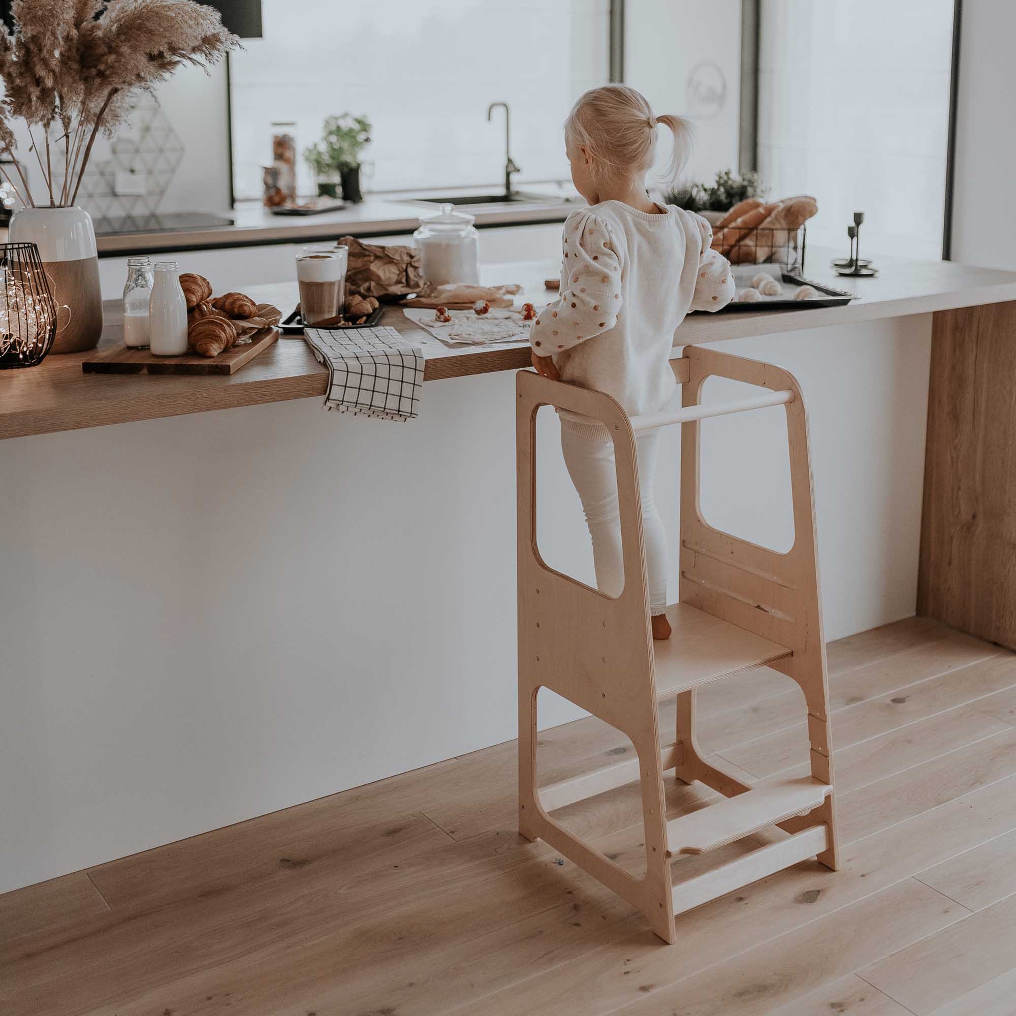 Toddler girl standing on a kids step stool in the kitchen