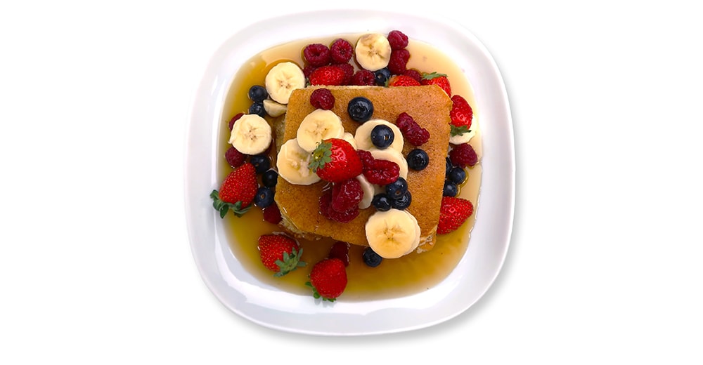 Vue du dessus d’une pile de pancakes avec des fruits rouges et des baies qui baignent dans une assiette de sirop d’érable.