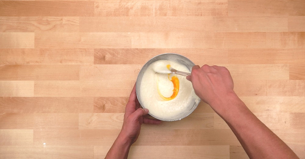 Les mains mélangent les blancs d’oeuf en incoporant le jaune d’œuf pour la préparation de la pâte à pancakes de Marge Simpson.