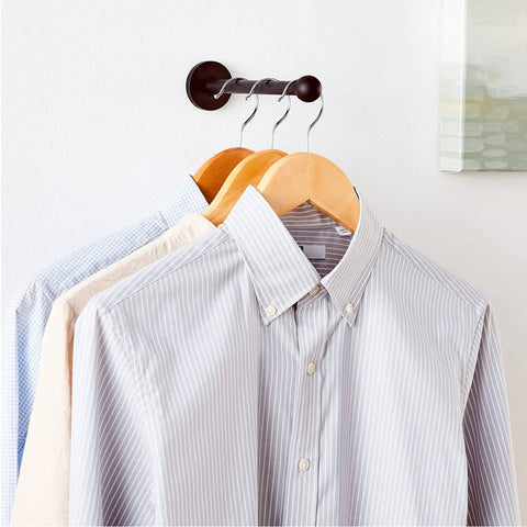 retractable brass garment rod holding 3 shirts on wood hangars