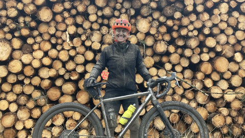 Muddy woman with bike infront of log pile