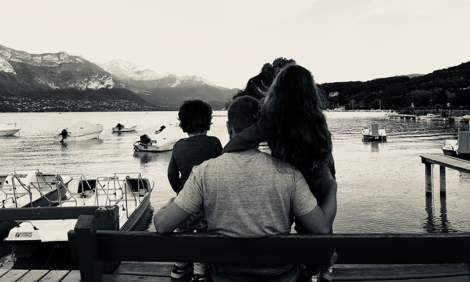 Papa avec sa fille et son fils sur un banc regardant les bateaux sur le lac et la montagne