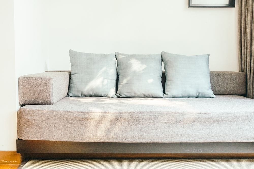 A gray couch suitable for dogs located in front of a window.