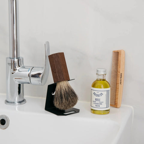 Razor brush sits by the side of the sink in a holder. It has a comb and a bottle of oil next to it.