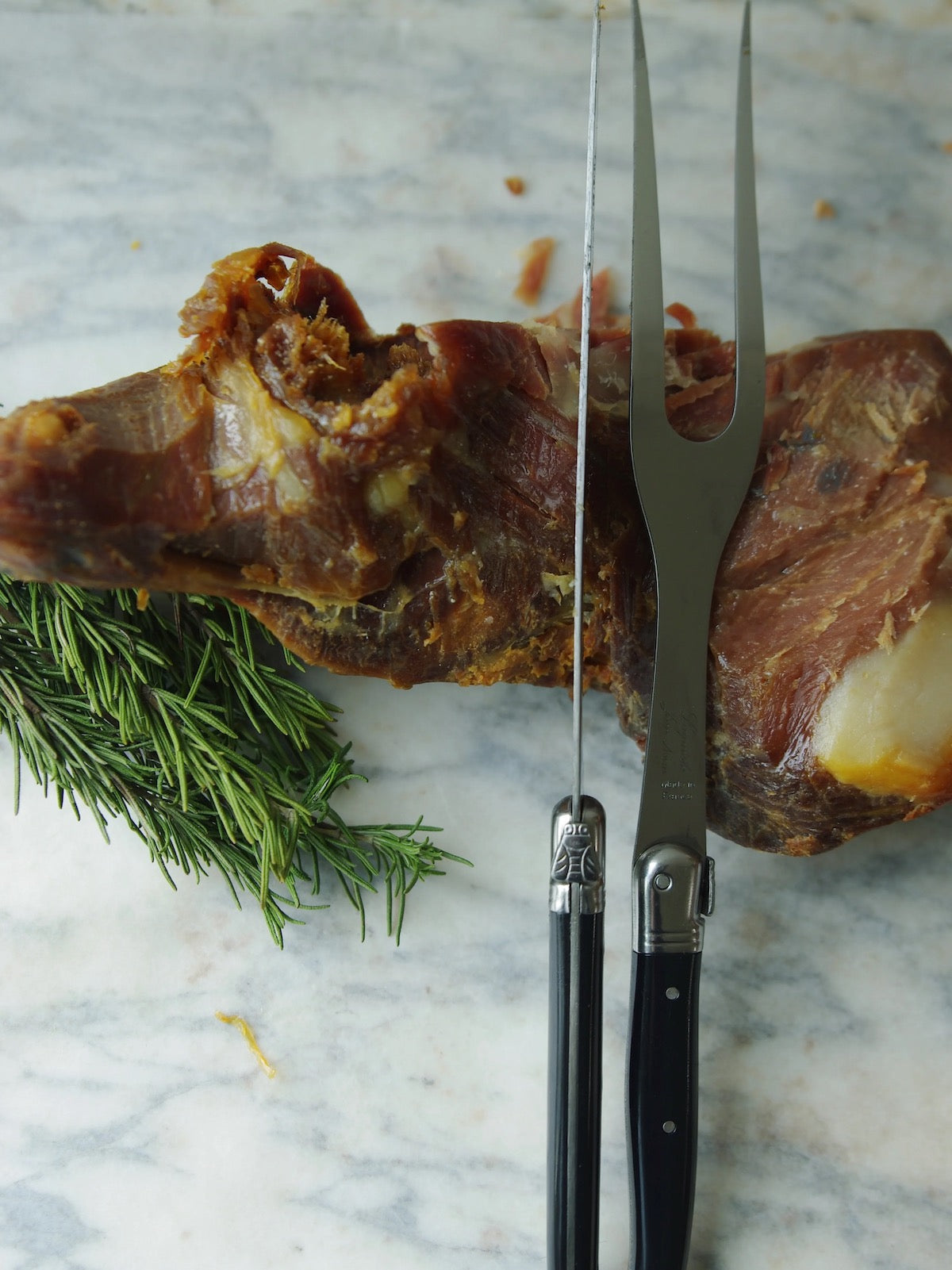 Black French carving set sits on a piece of meat on a marble background