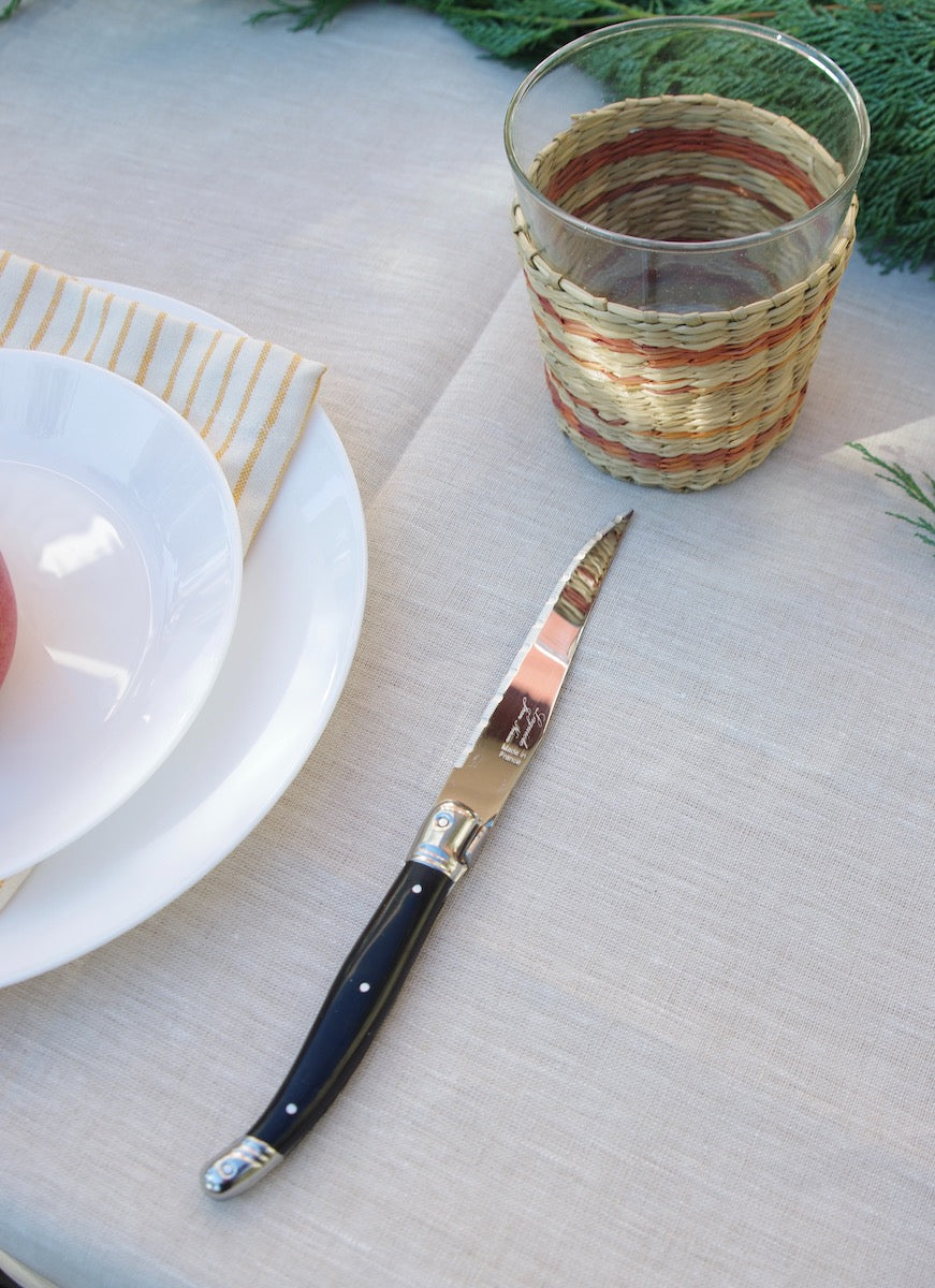 Seagrass glass next to black knife on linen tablecloth