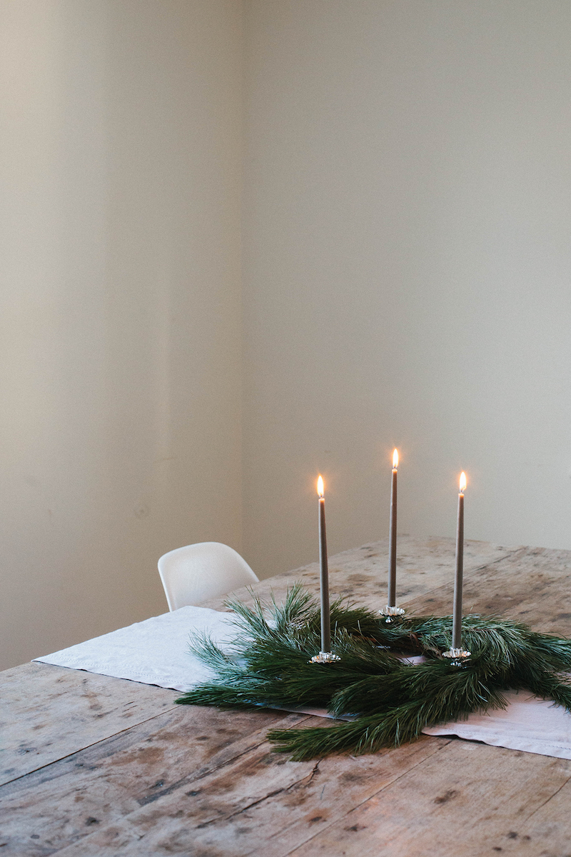 Candles sit in a wreath on a wooden table