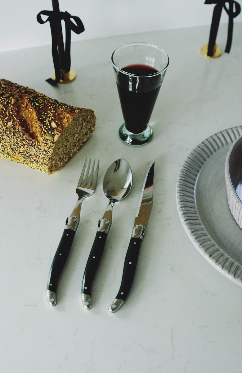 Black Laguiole fork, spoon, and knife on white countertop