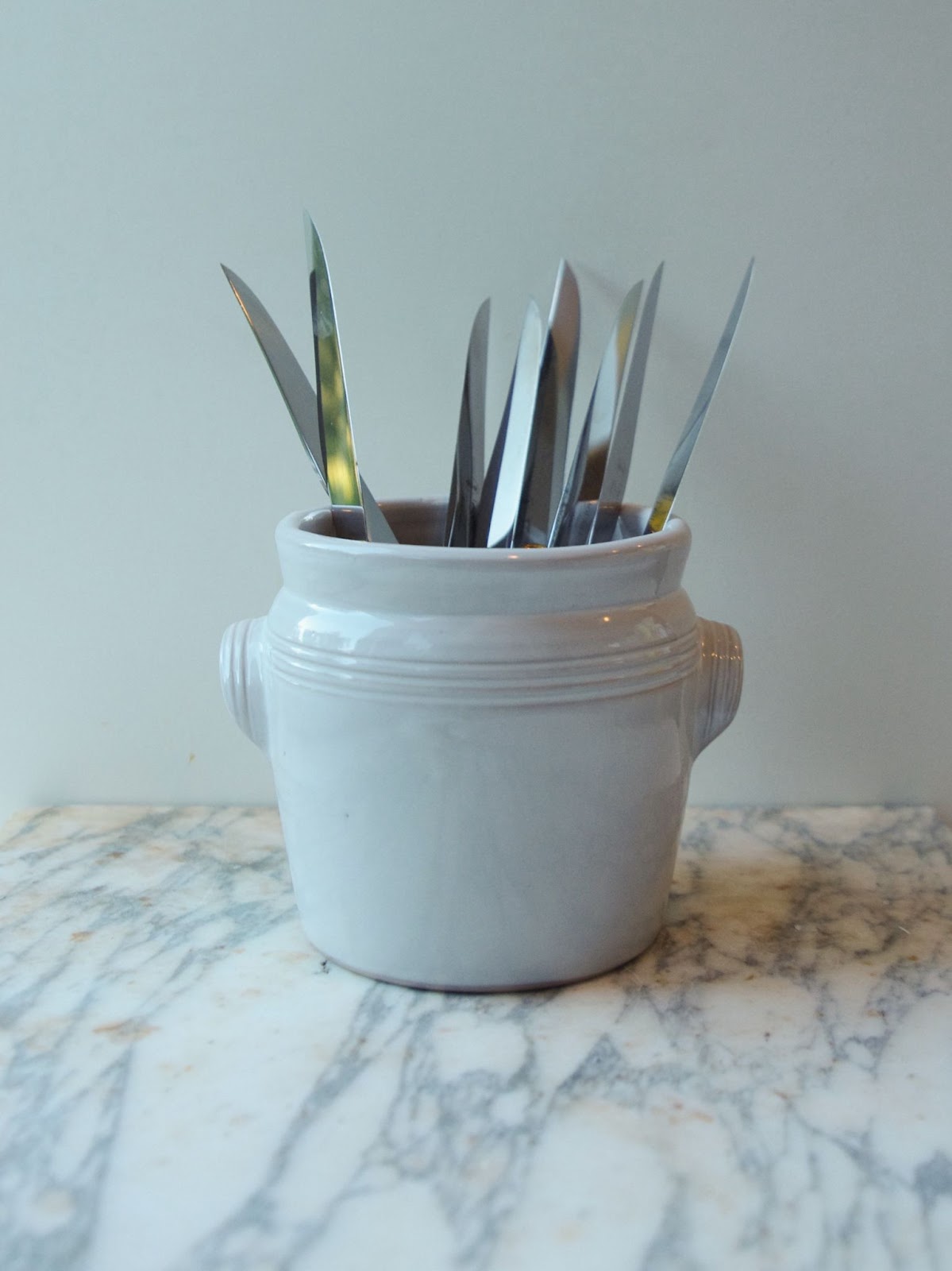 White cutlery crock with two handles holding knives.