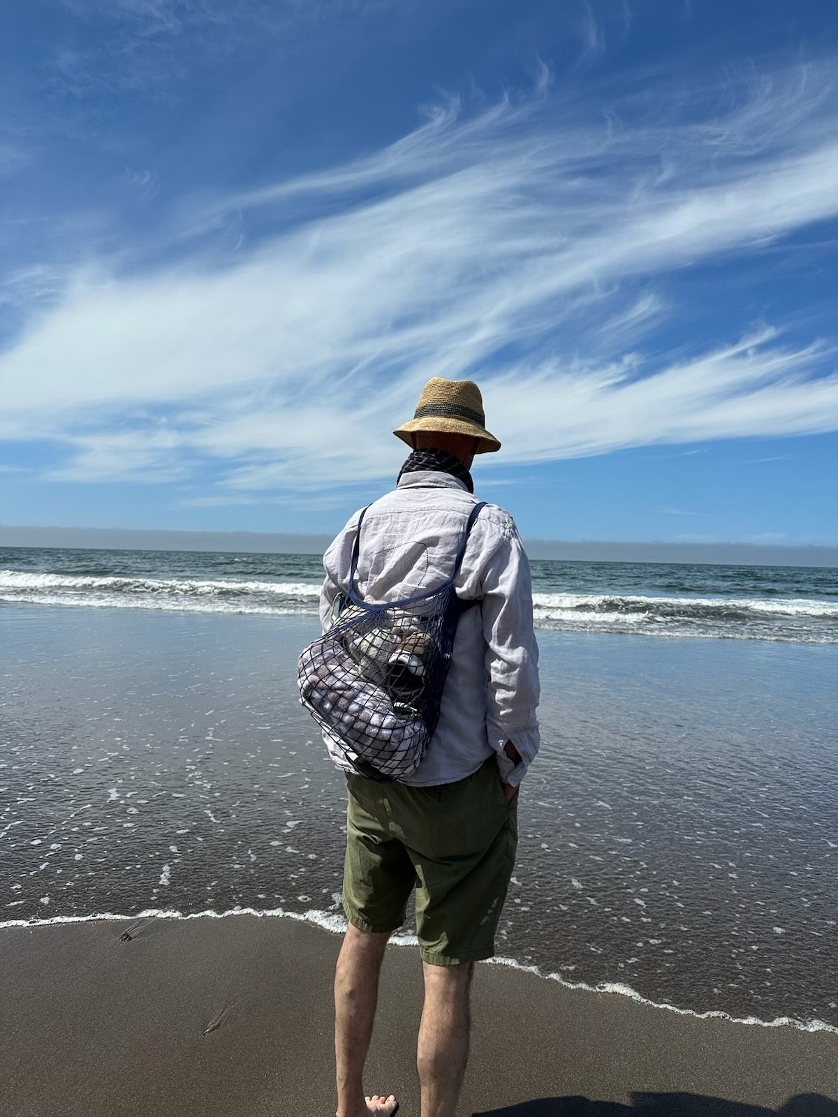 Man standing on beach using net tote bag as a backpack.