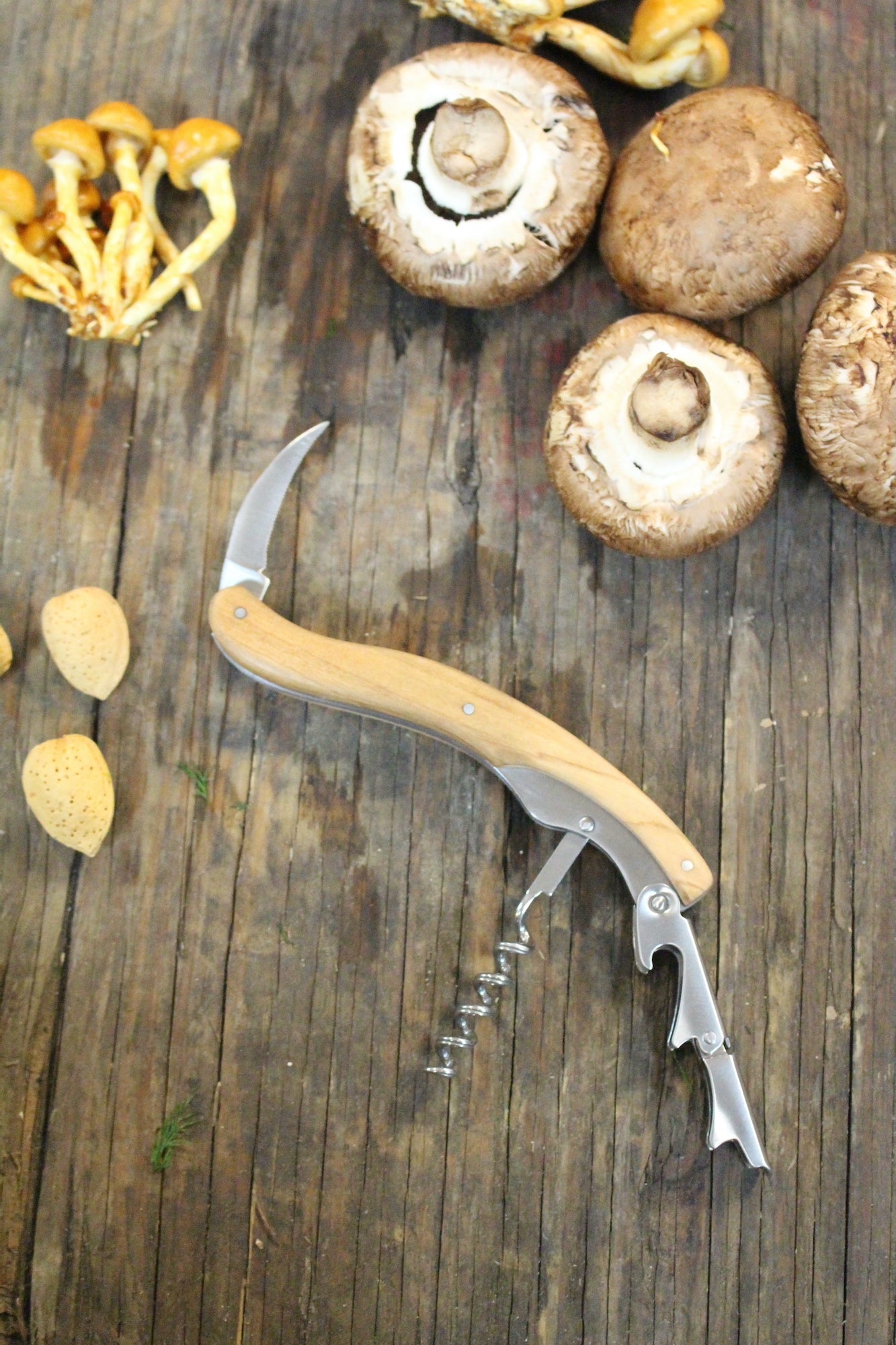 Olivewood corkscrew next to mushrooms on wooden table.