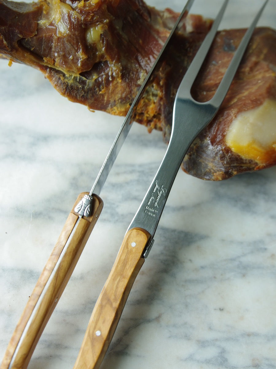 An olive wood carving set sits on a piece of dried meat, waiting to be cut.