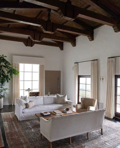 Living room with two large white couches and brown wooden beams.