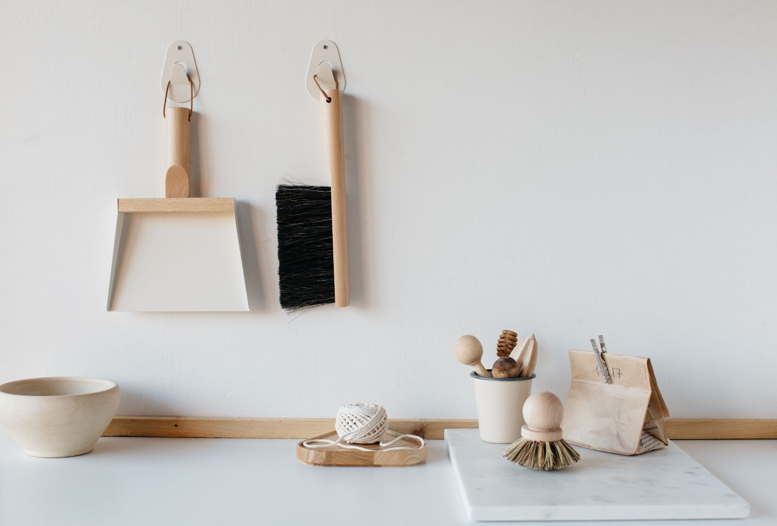 White dustpan and wooden hand broom hanging on wall above office desk.