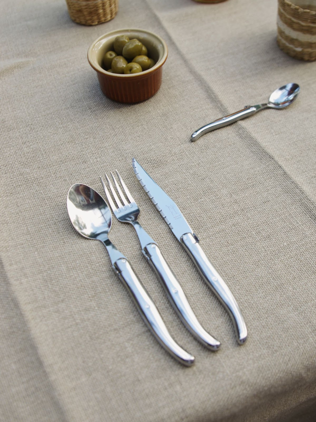 Ramekin, stainless steel Laguiole spoon, fork, knife and coffee spoon on linen tablecloth.