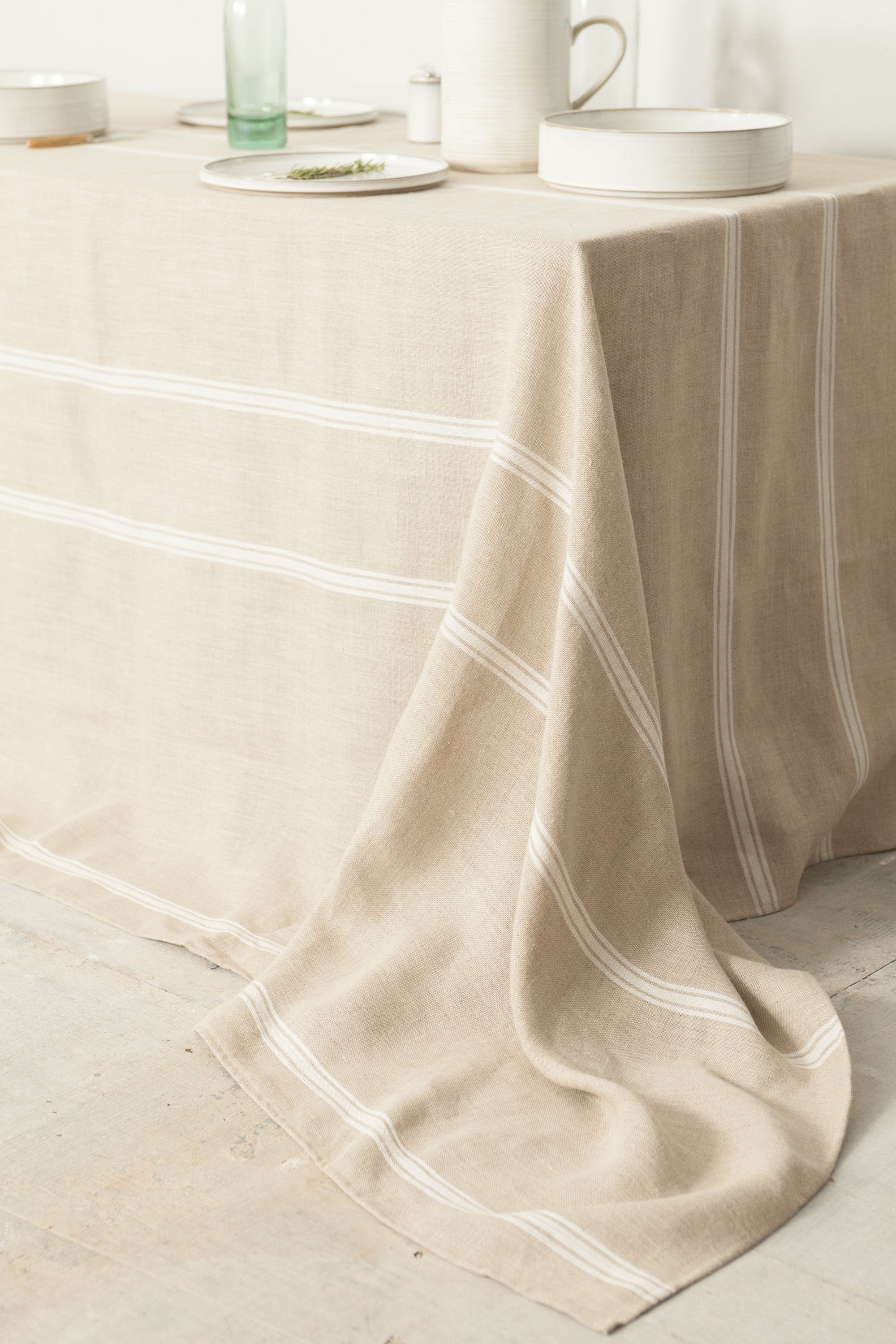 Linen tablecloth with horizontal white stripes. Tablescape features white ceramic dinnerware and green glass.