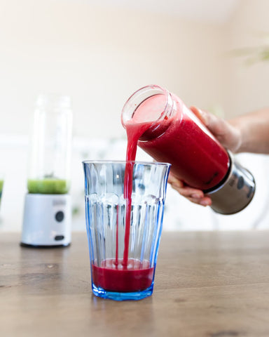 Blended red berry breakfast smoothie pouring into a glass