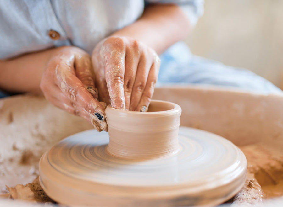 A detailed image of a pair of hands delicately sculpting clay on a potter's  wheel during a soft-lit evening in a pottery studio, captured with a medium  format camera using a macro