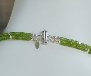 Hammered silver abstract pendant necklace with two strands of faceted peridot and silver beads. The necklace is finished with a magnetic clasp and the artist's signature tag. The necklace measures 17" (43.18cm). The necklace is displayed on a white mannequin neck showing a closeup of the clasp.