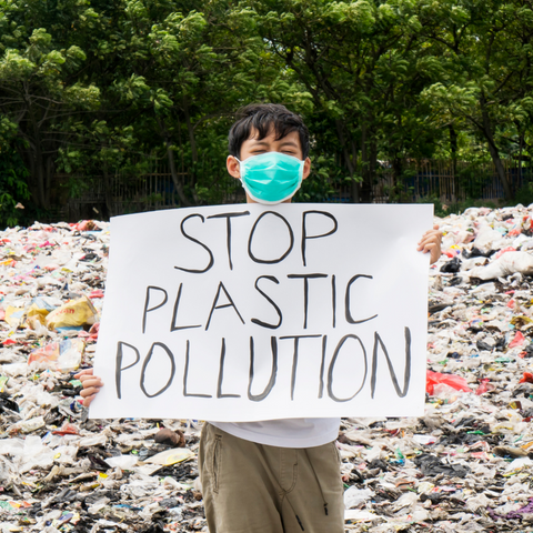 Image of a boy standing in lots of plastic and holding up a sign that says 'stop plastic pollution' in capital letters.