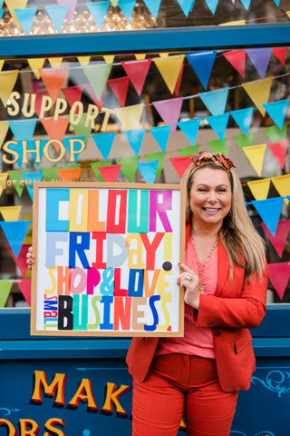 Holly Tucker holding up Colour Friday poster outside shop