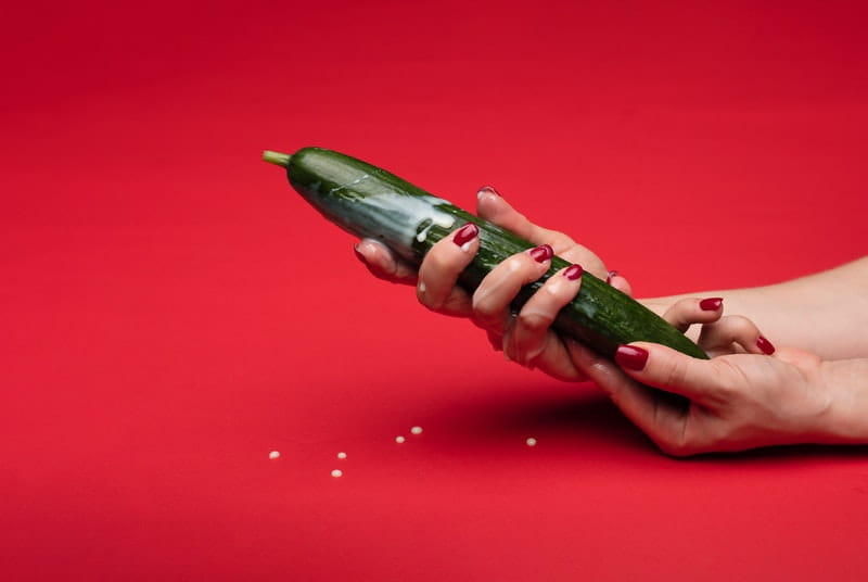 Woman stroking creamy zucchini to represent ejaculating penis