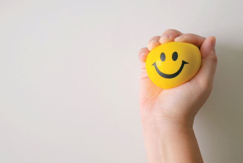 Happy face ball being squeezed to represent happiness from squeeze technique