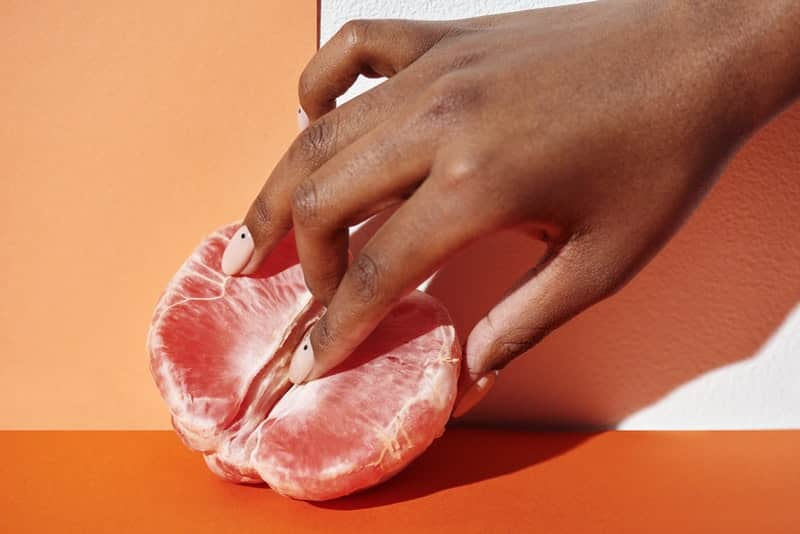 Woman demonstrating yoni massage technique on frozen orange half