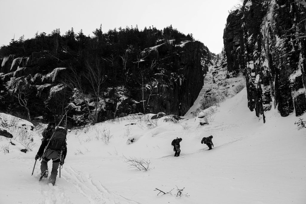 Black and white photo of three climbers approaching a snowy, rocky pass