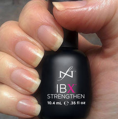 This show a right hand holding a bottle of the strengthen product. It is in a black bottle, resembling a nail polish bottle, with white and pink writing. This is the second step of the IBX® process.   The nails are approximately 1/4 inch long and look strong and healthy. No polish has applied after receiving IBX® treatment.