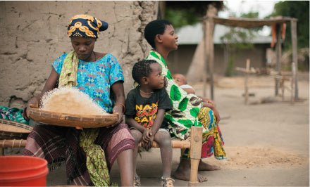 An African mother prepares a meal while her two young sons wait next to her