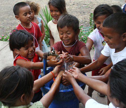Group of young children enjoy washing their hands in clean water from a community water pump