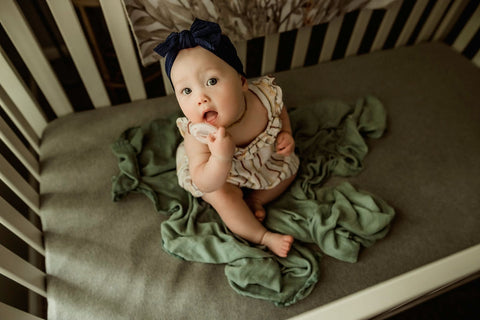 Infant girl sits in her crib with Ninni pacifier and blanket