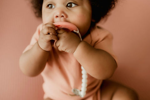 Baby sitting up and using hands to hold ninni pacifier in mouth