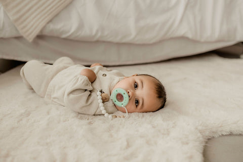 Young infant lying on bed with eyes open and Ninni pacifier