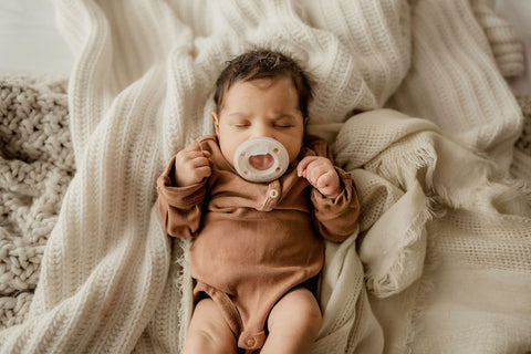 Young infant lying on bed with eyes closed and Ninni pacifier