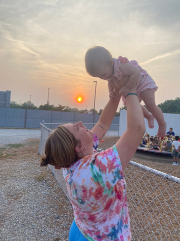 Happy mom joyfully lifts infant daughter in the air while outside at a ballfield