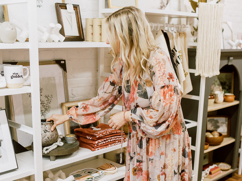 Amber wearing a floral pink dress placing curated home goods on the shelf at Pink Lemon Decor