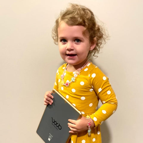 image of a little girl in a dress holding an ipad with a WaveBlock EMF protection sticker on it