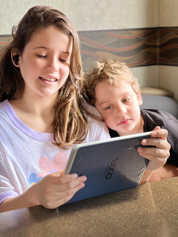 a young boy and girl sitting next to each other with an ipad in between them looking at it together. There is WaveBlock EMF protection sticker on the back of the iPad.