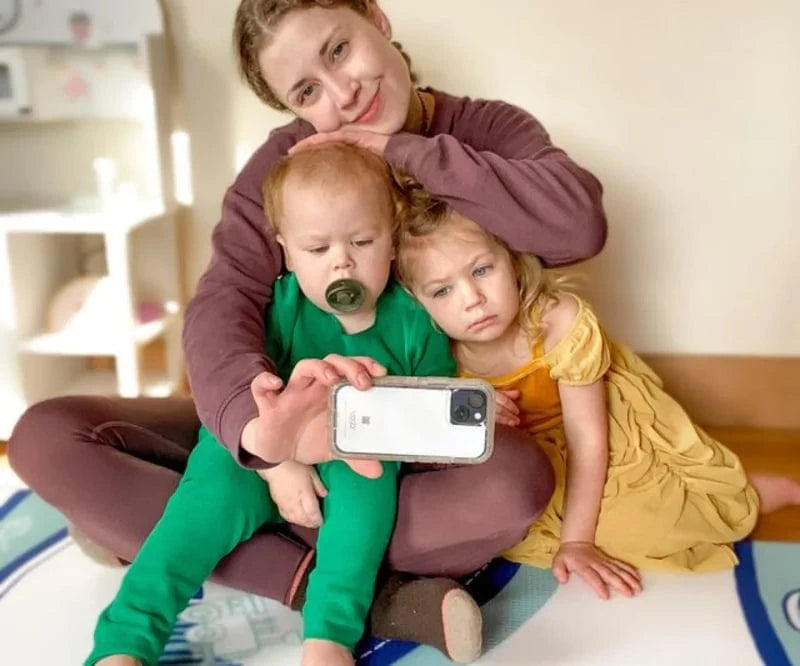 A woman taking a selfie with two young children, one with a pacifier.