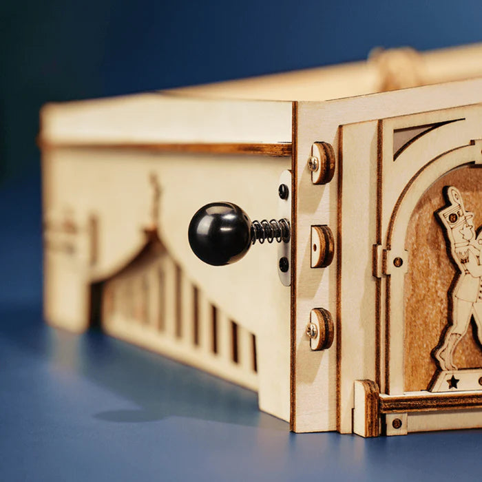 Close-up of a wooden mechanical toy with a crank handle and intricate engravings.