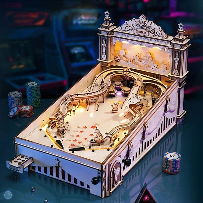 Wooden miniature pinball machine model with lights, surrounded by poker chips.