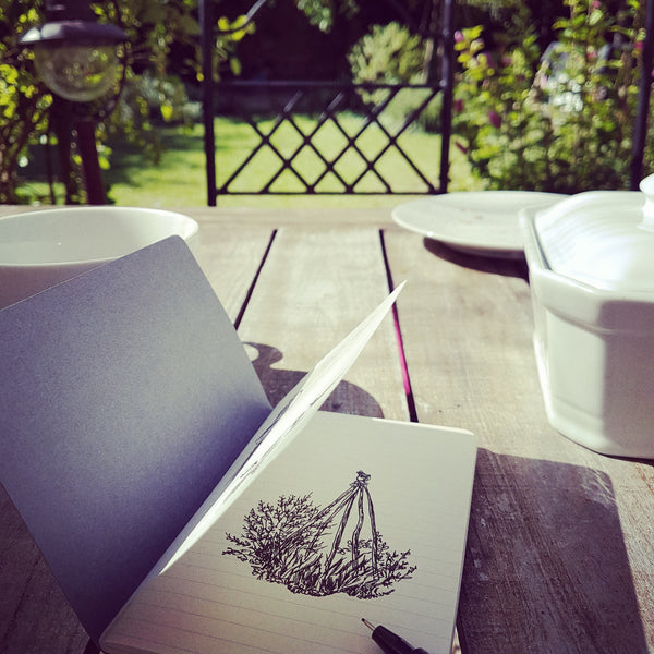 Sketchbook open with a fineliner drawing on the page, on a garden table