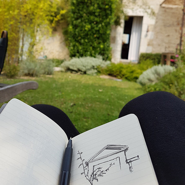 Sketchbook open with fineliner drawing on the page, in front of a beautiful French country house